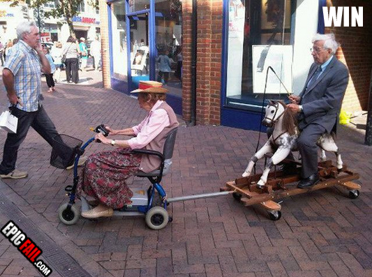 Une veille dame en fauteuil roulant lectrique avec remorque... sur la remorque : un vieil homme en costume trois pice assis sur un poney balanoire